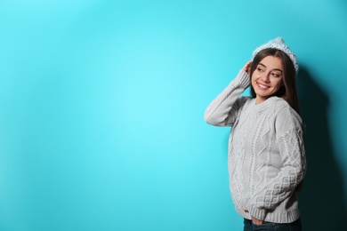 Beautiful young woman in warm sweater with hat on color background. Space for text