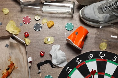 Food leftovers, shoes and elements of different games after party on wooden floor, flat lay