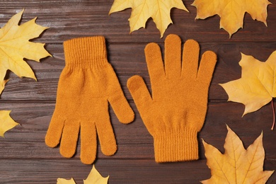 Photo of Stylish orange woolen gloves and dry leaves on wooden table, flat lay