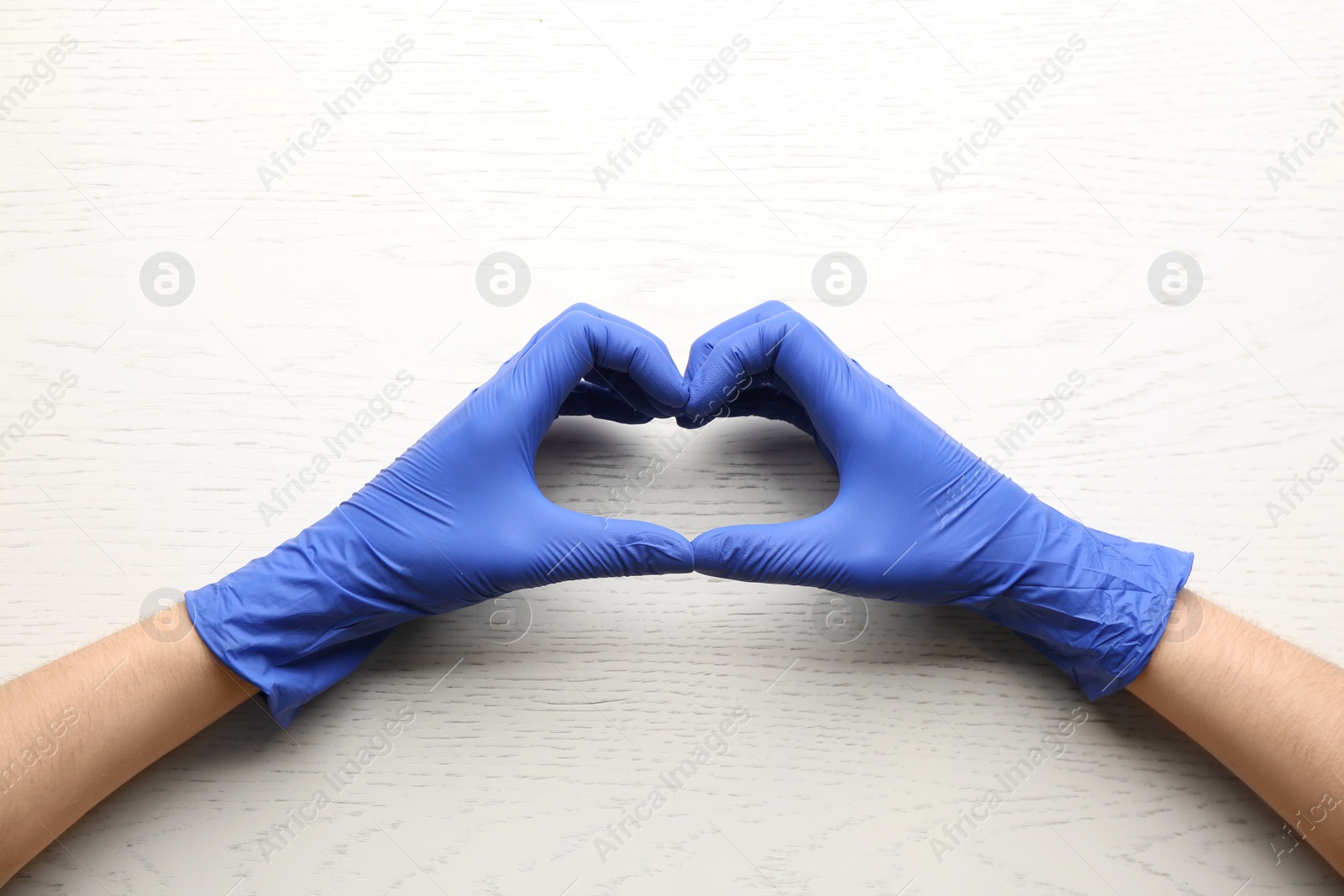 Photo of Person in medical gloves showing heart gesture on white wooden background, closeup of hands