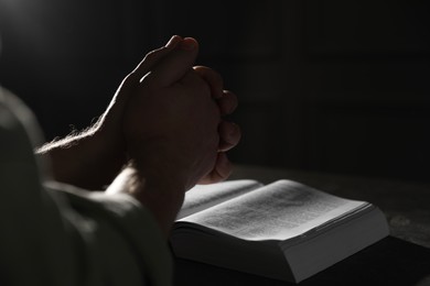 Photo of Religion. Christian man praying over Bible at table, closeup. Space for text