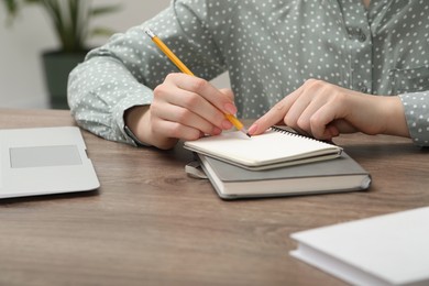 Photo of Woman writing in notebook at wooden table indoors, closeup