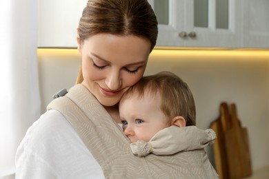 Mother holding her child in sling (baby carrier) at home