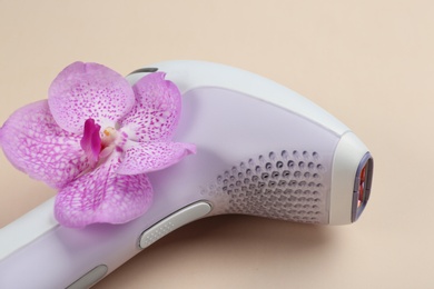 Modern photoepilator with orchid flower on beige background, closeup