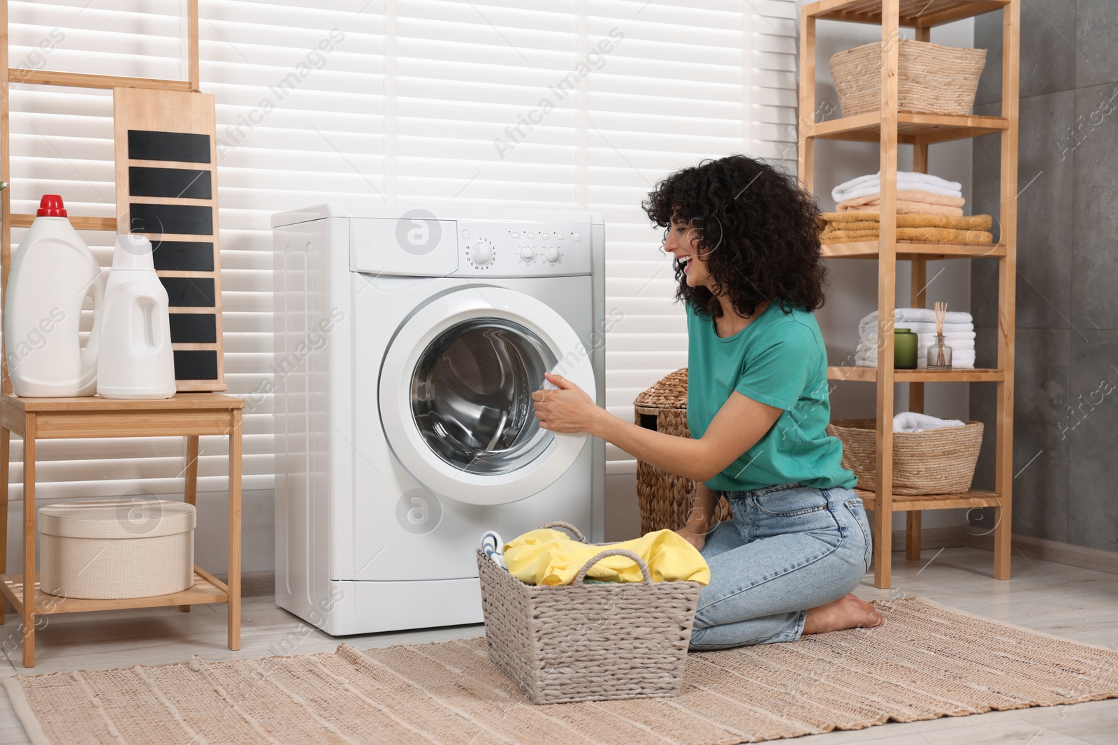 Photo of Happy woman with laundry near washing machine indoors