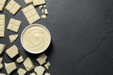 Photo of Tasty white chocolate paste in bowl and pieces on black table, flat lay. Space for text