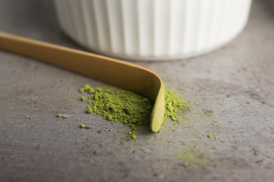 Photo of Green matcha powder and bamboo scoop on light grey table, closeup