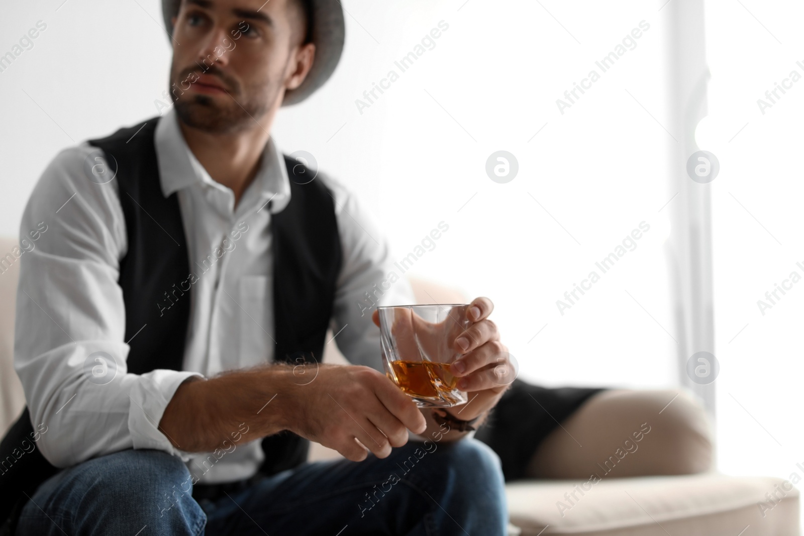 Photo of Young man with glass of whiskey sitting on sofa at home