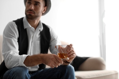 Photo of Young man with glass of whiskey sitting on sofa at home