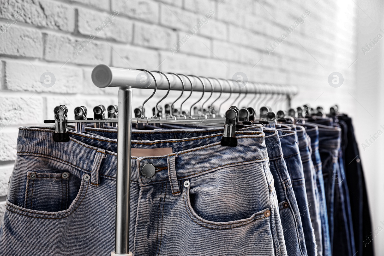 Photo of Rack with stylish jeans near brick wall, closeup