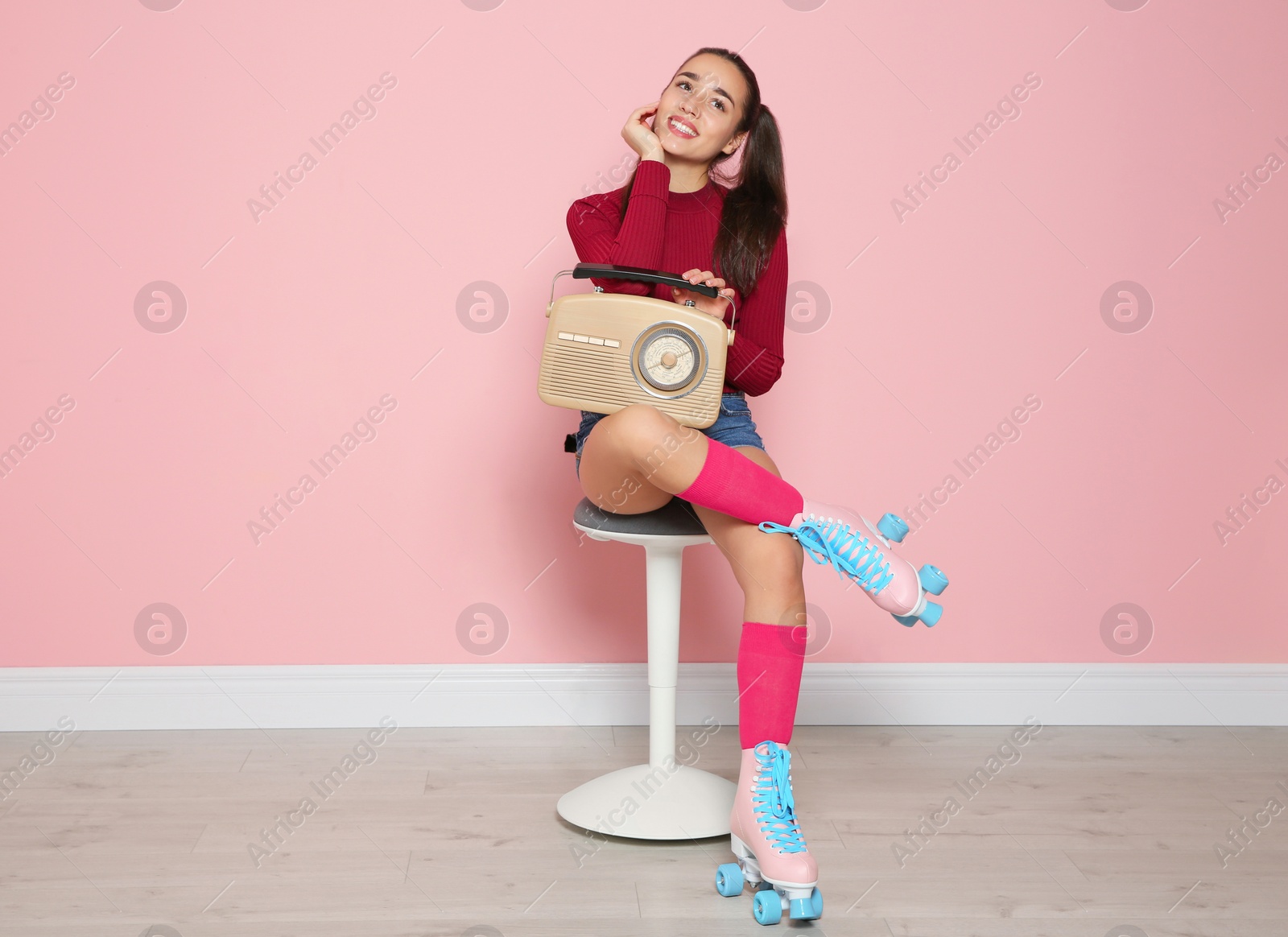 Photo of Young woman with roller skates and retro radio sitting on chair near color wall