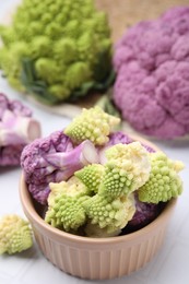 Photo of Various cauliflower cabbages on white tiled table, closeup