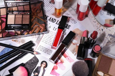 Photo of Bright lip glosses among different cosmetic products and fashion magazine on table