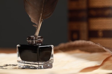 Inkwell with feather and vintage parchments on table, closeup. Space for text