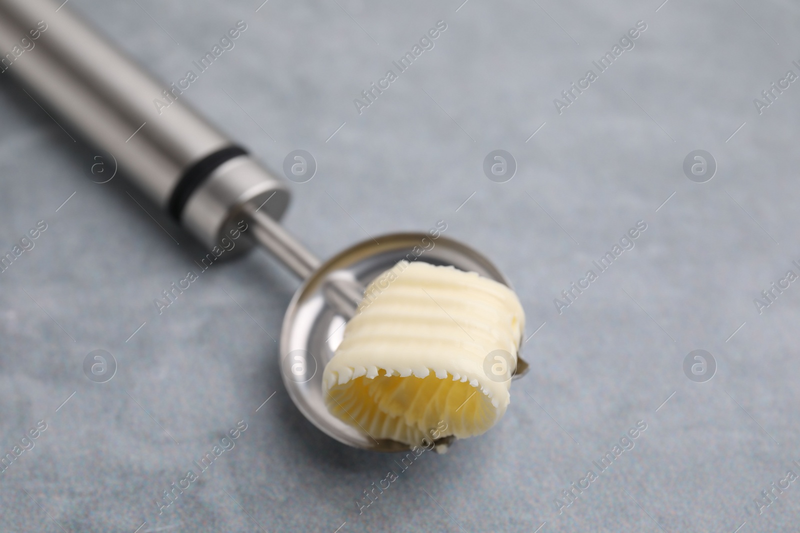 Photo of Tasty butter curl in spoon on light grey table, closeup. Space for text