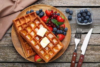 Photo of Plate of delicious Belgian waffles with honey, berries and butter on wooden table, flat lay