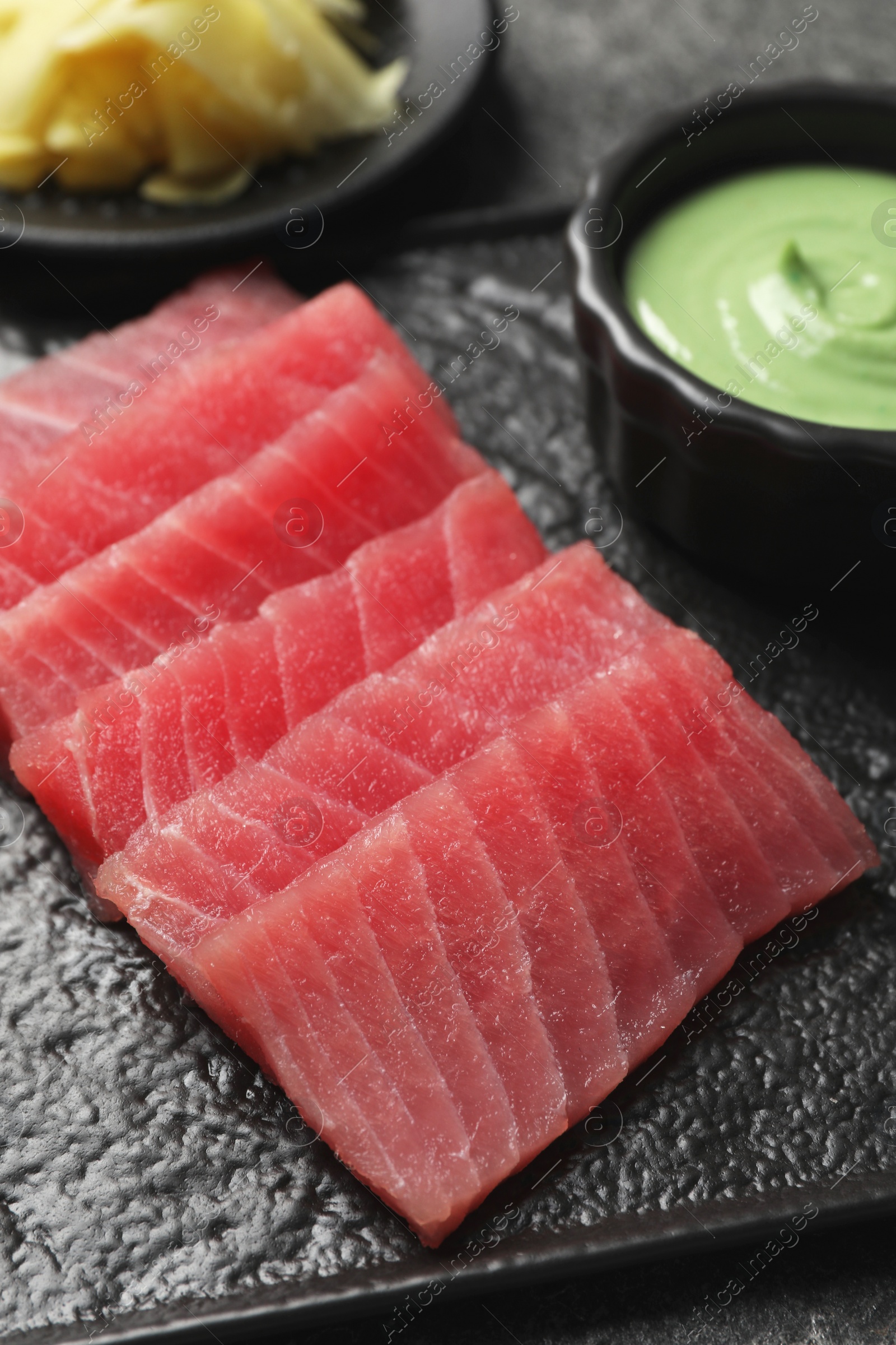 Photo of Tasty sashimi (pieces of fresh raw tuna) on black plate, closeup