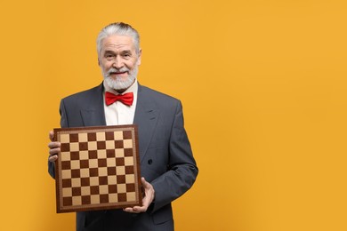 Man with chessboard on orange background, space for text. Intellectual game
