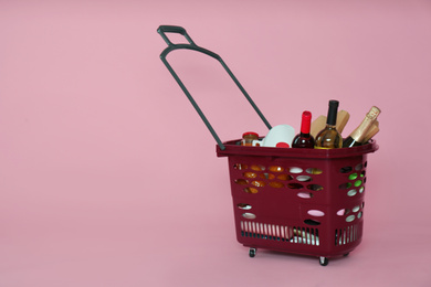 Photo of Shopping basket full of different products on pink background. Space for text
