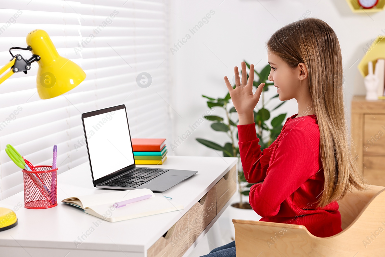 Photo of E-learning. Cute girl raising her hand to answer during online lesson at table indoors