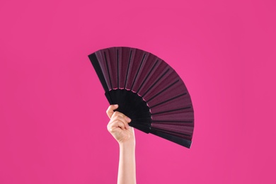 Photo of Woman holding black hand fan on pink background, closeup