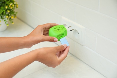 Photo of Woman putting insect repellent plate into electric mosquito device at home, closeup