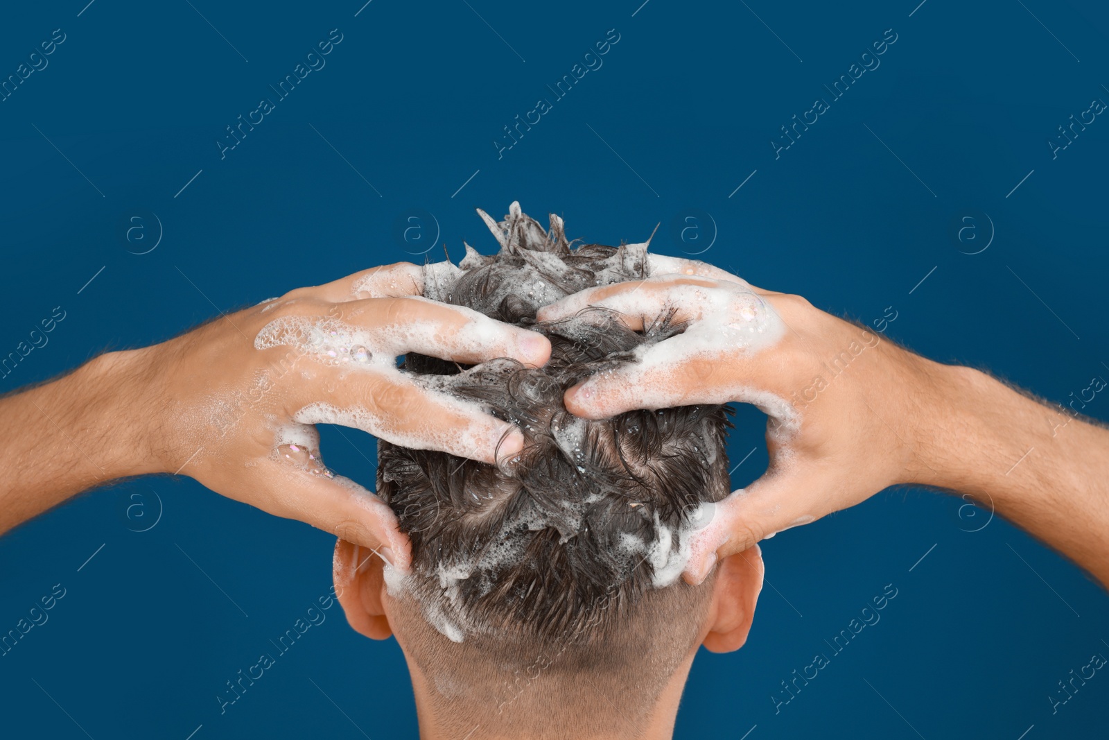 Photo of Man washing hair on blue background, closeup