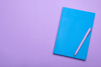 Photo of Light blue notebook and pen on lilac background, top view. Space for text