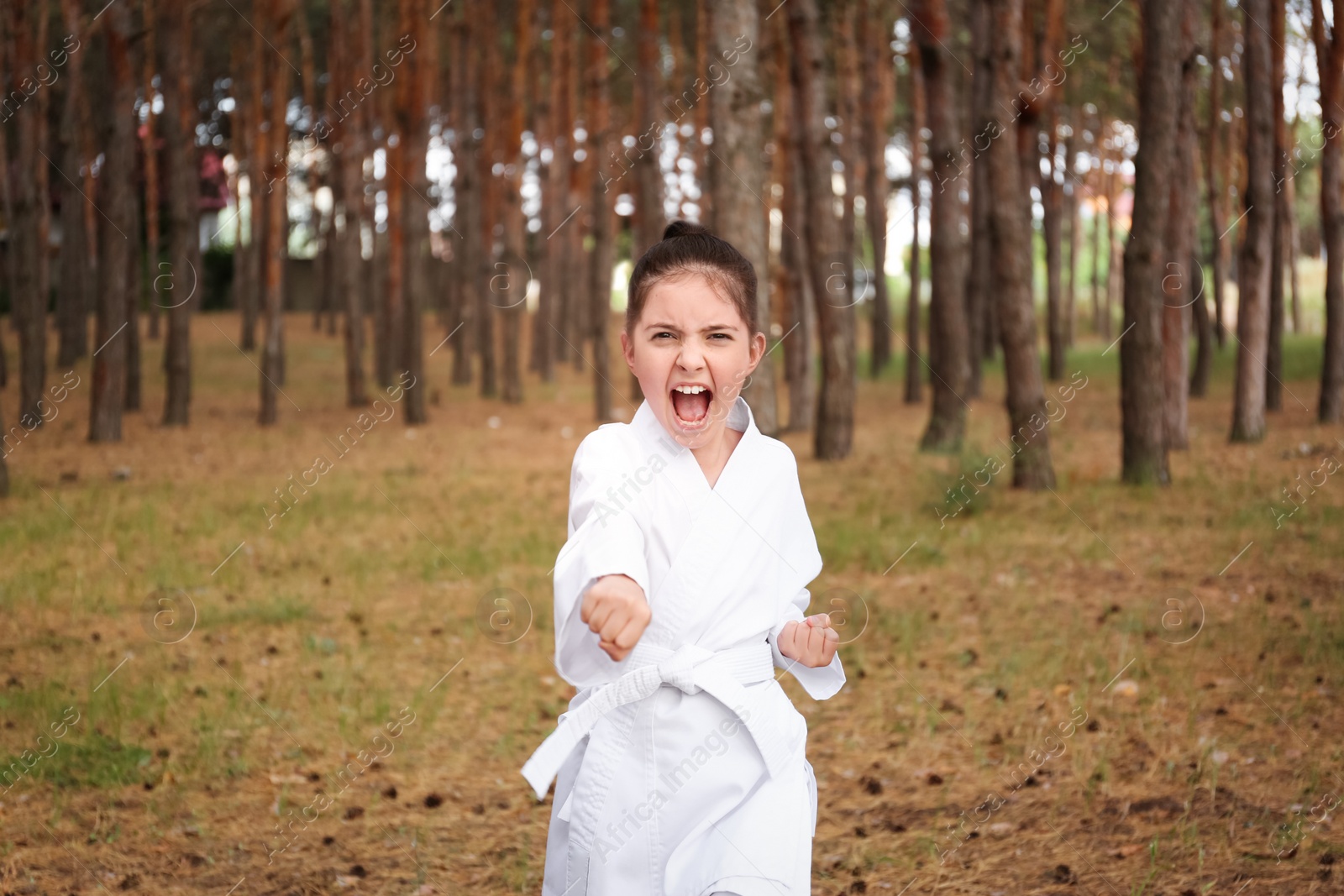 Photo of Cute little girl in kimono practicing karate in forest