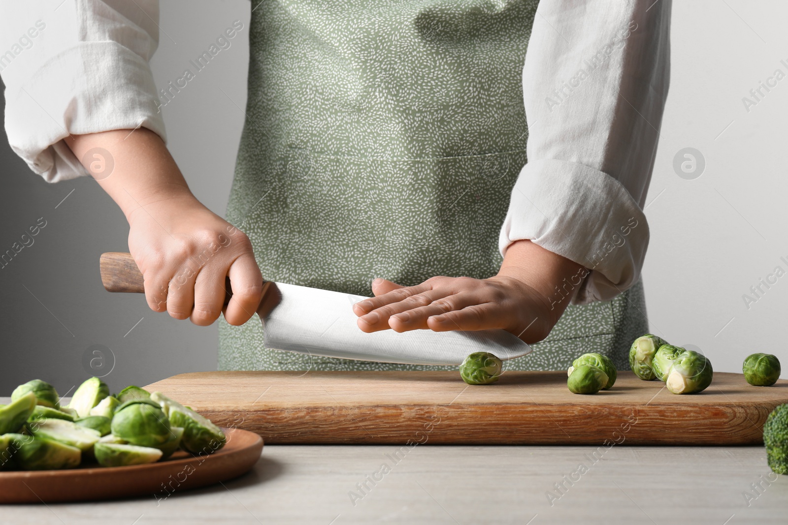 Photo of Woman cutting fresh brussel sprouts on board at wooden table, closeup