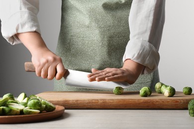 Photo of Woman cutting fresh brussel sprouts on board at wooden table, closeup
