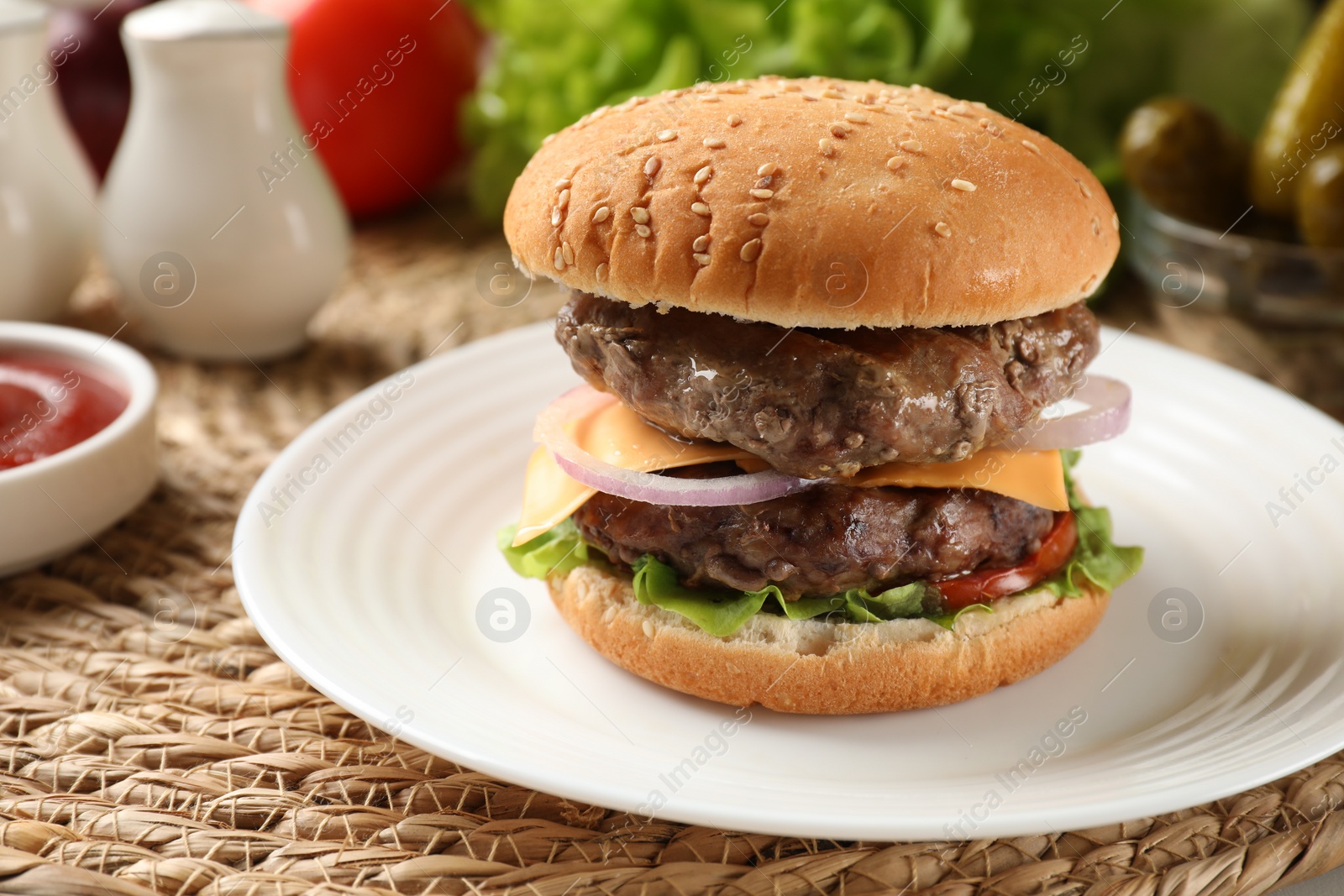 Photo of Tasty hamburger with patties, cheese and vegetables on wicker mat, closeup