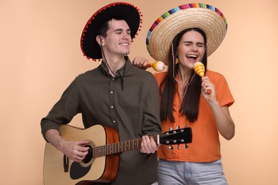 Photo of Lovely couple woman in Mexican sombrero hats with maracas and guitar on beige background