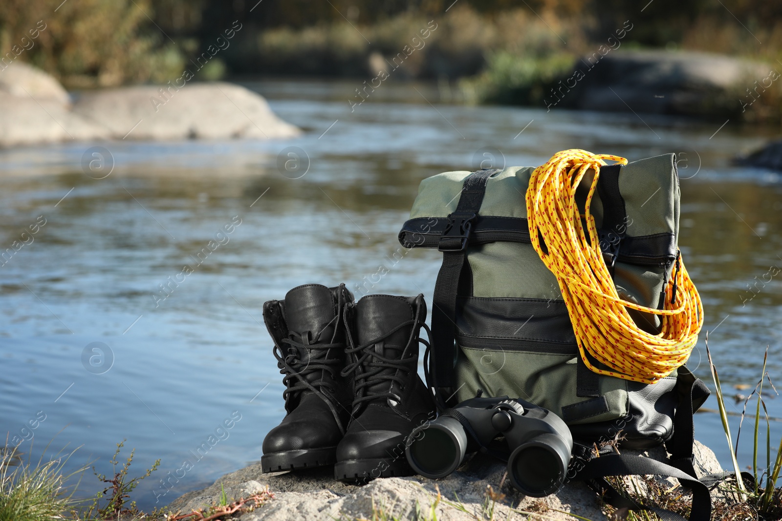 Photo of Set of camping equipment on rock near pond outdoors. Space for text