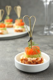 Photo of Tasty canape with salmon, cucumber, bread and cream cheese on grey table, closeup