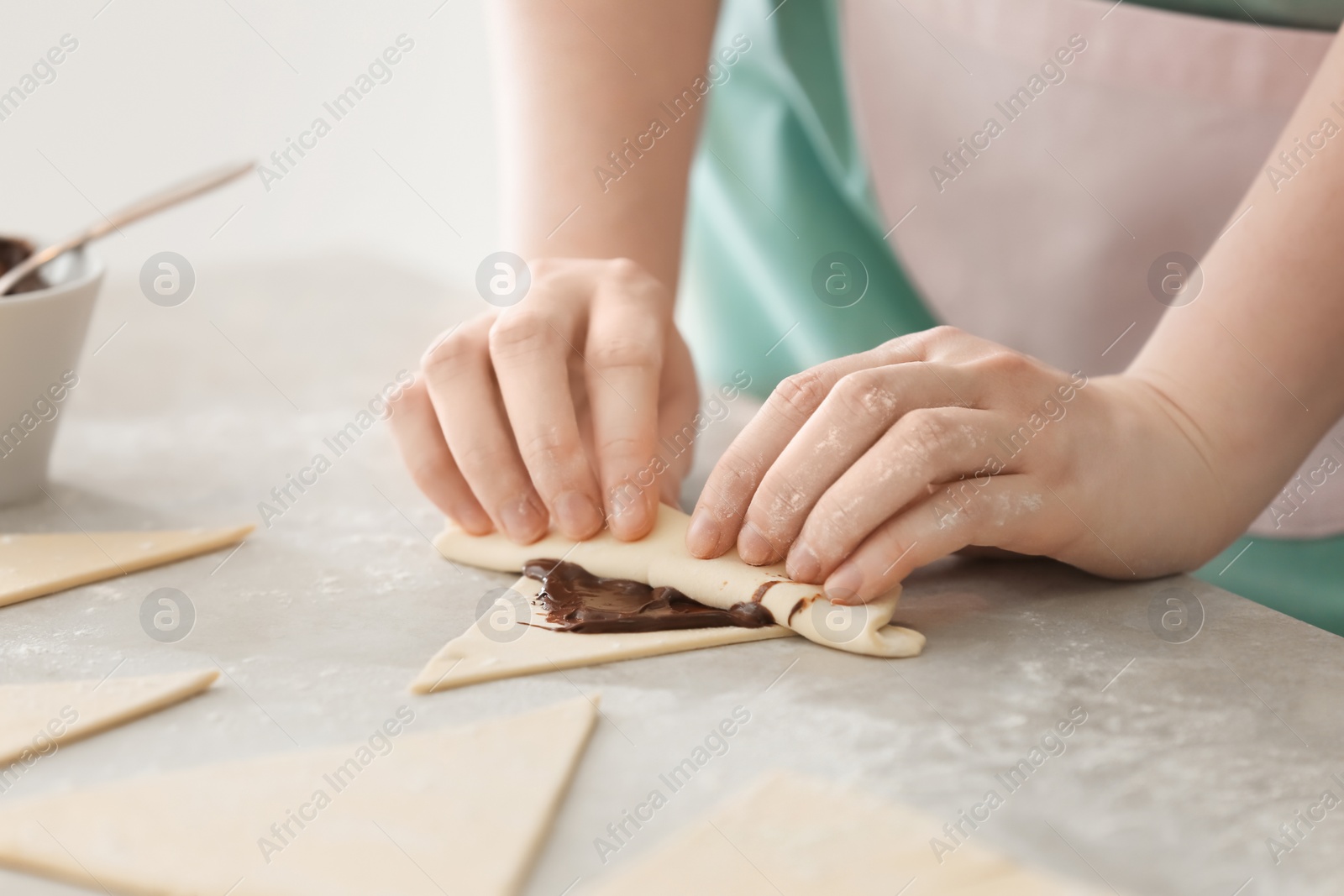 Photo of Woman preparing tasty croissants with chocolate paste on table, closeup