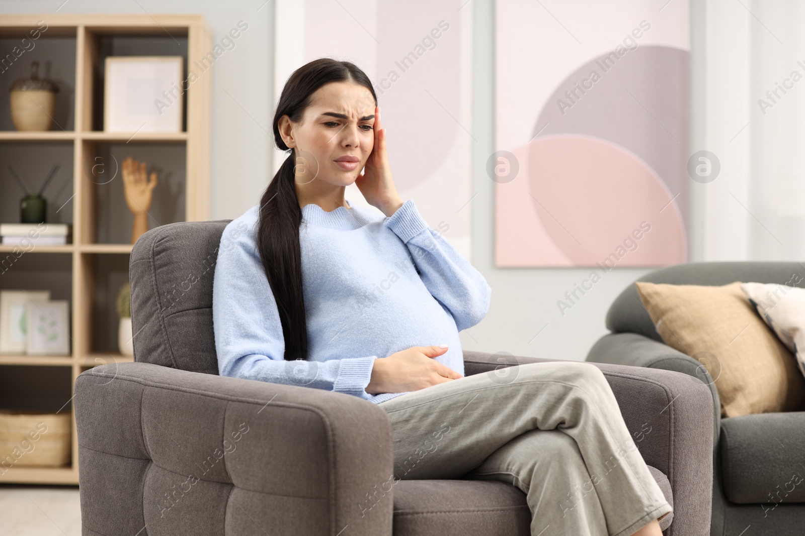 Photo of Pregnant woman suffering from headache on armchair at home