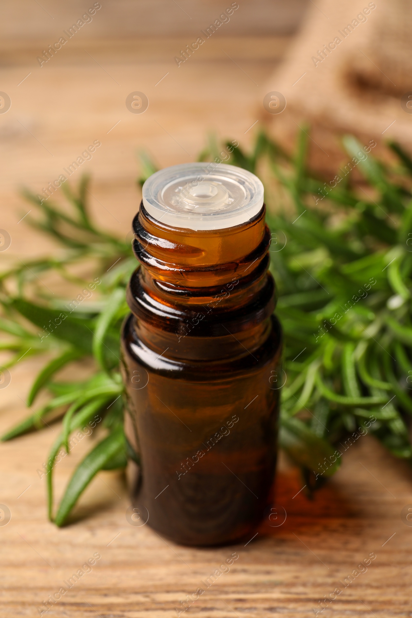 Photo of Bottle with essential oil and fresh rosemary on wooden table, closeup