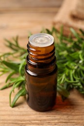 Photo of Bottle with essential oil and fresh rosemary on wooden table, closeup