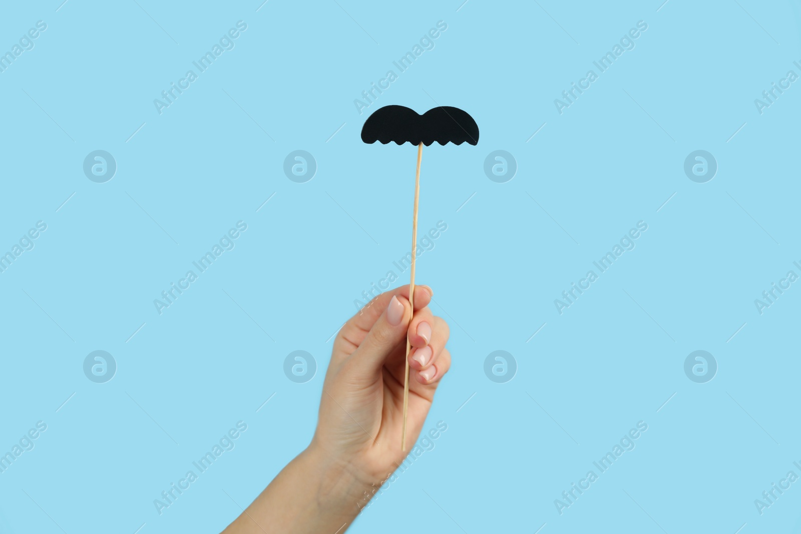 Photo of Woman with fake paper mustache on light blue background, closeup