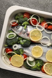 Photo of Raw fish with vegetables and lemon in baking dish on grey table, top view