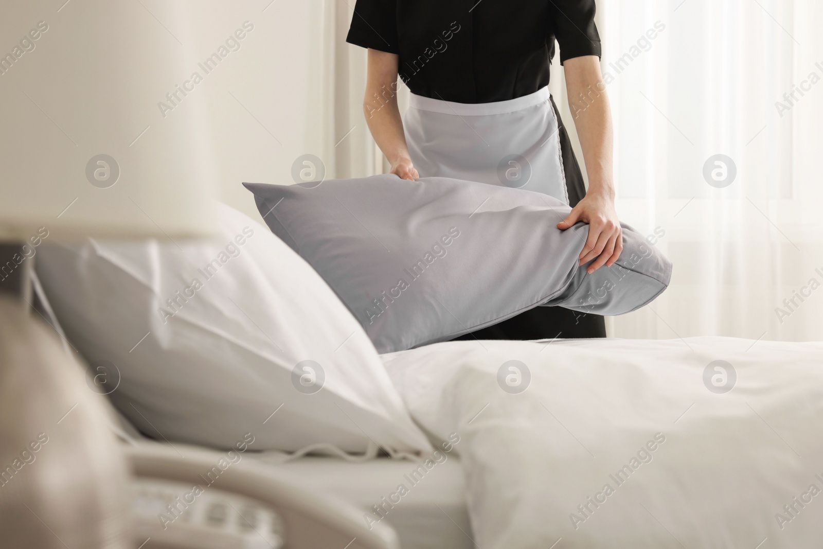 Photo of Young maid making bed in hotel room, closeup