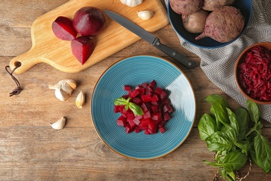 Plate of cut boiled beets with basil and garlic on wooden table, flat lay