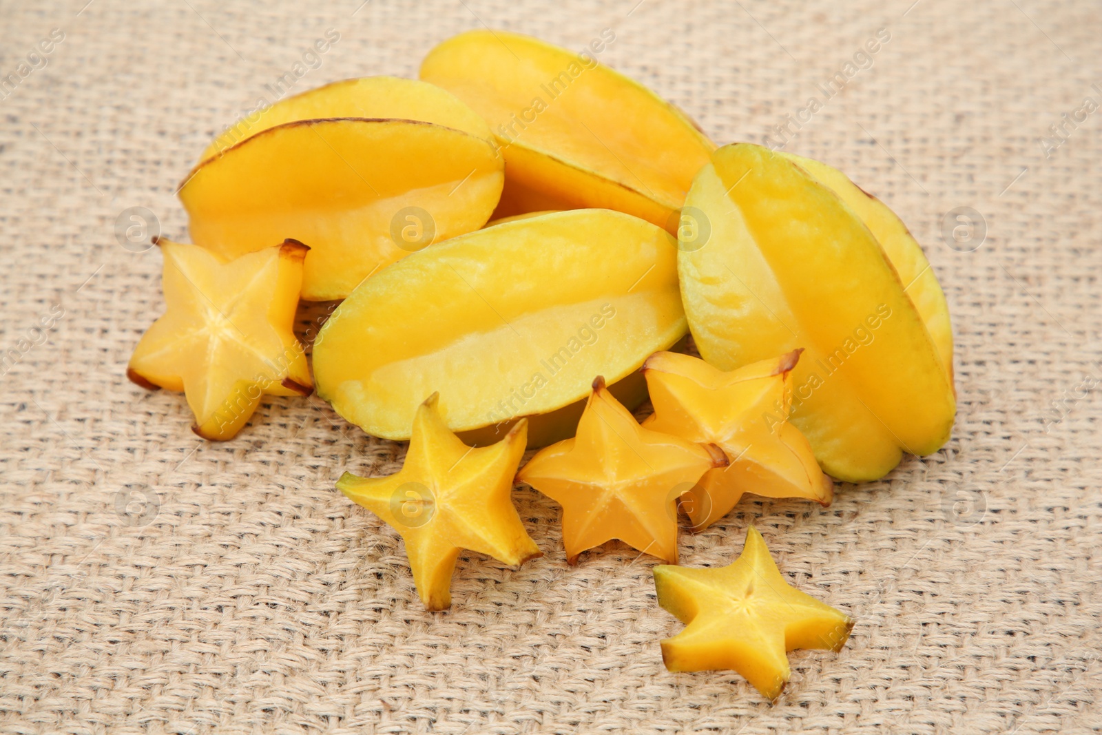 Photo of Cut and whole delicious ripe carambolas on burlap fabric