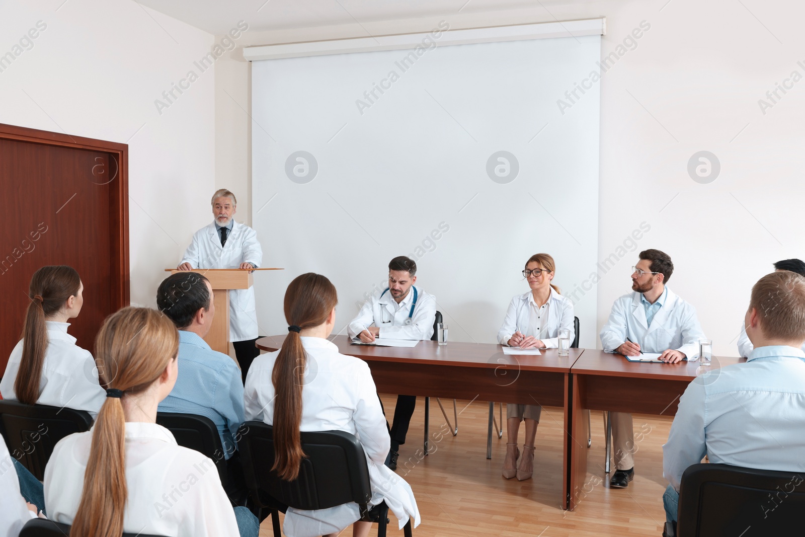 Photo of Senior doctor giving lecture in conference room with projection screen