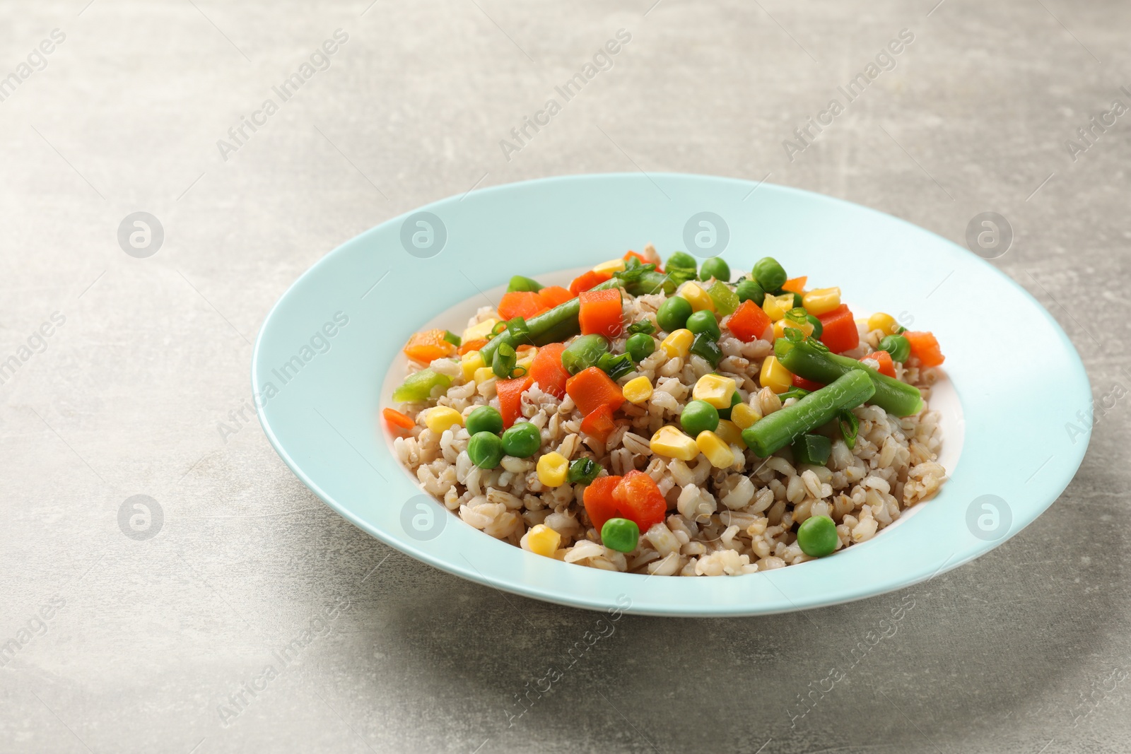 Photo of Tasty pearl barley porridge with vegetables on light textured table, closeup