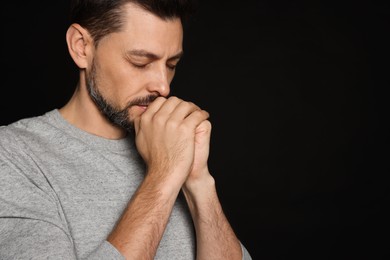Man with clasped hands praying on black background. Space for text