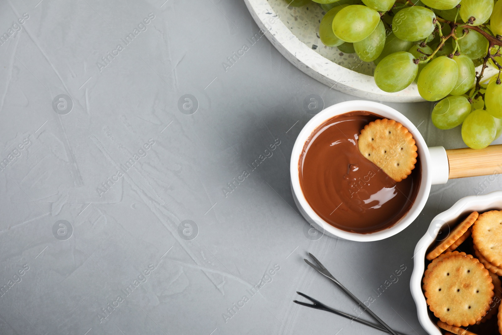 Photo of Dipping cookie into pot with chocolate fondue on grey table, flat lay. Space for text