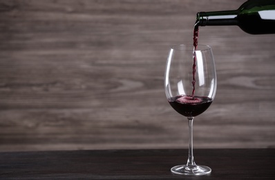 Pouring wine from bottle into glass on table against wooden background, space for text