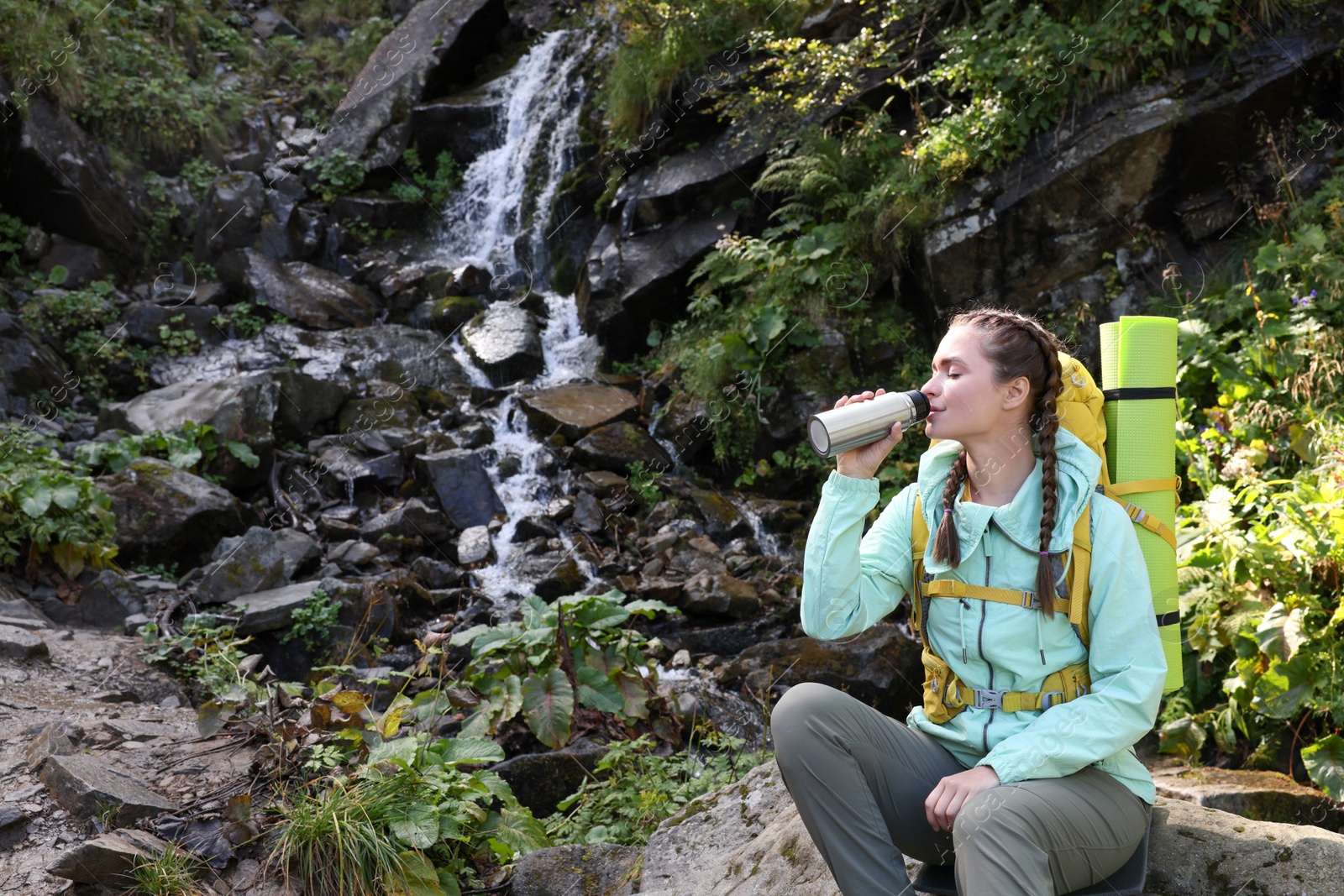 Photo of Tourist with vacuum flask near waterfall in mountains. Space for text